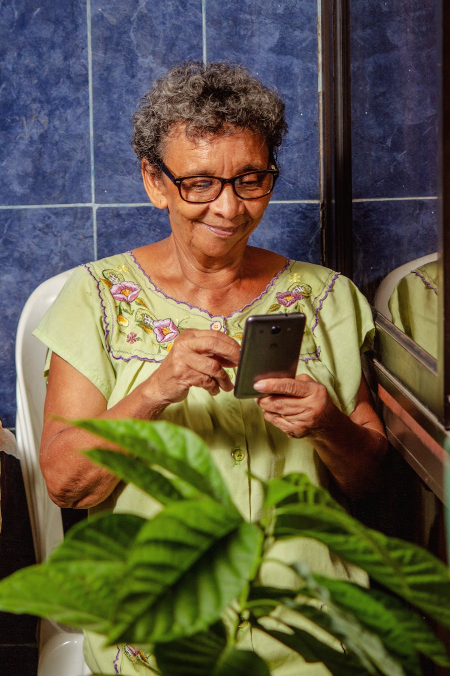 An older woman who lives alone, smiling as she reads a hug on her phone at her kitchen table